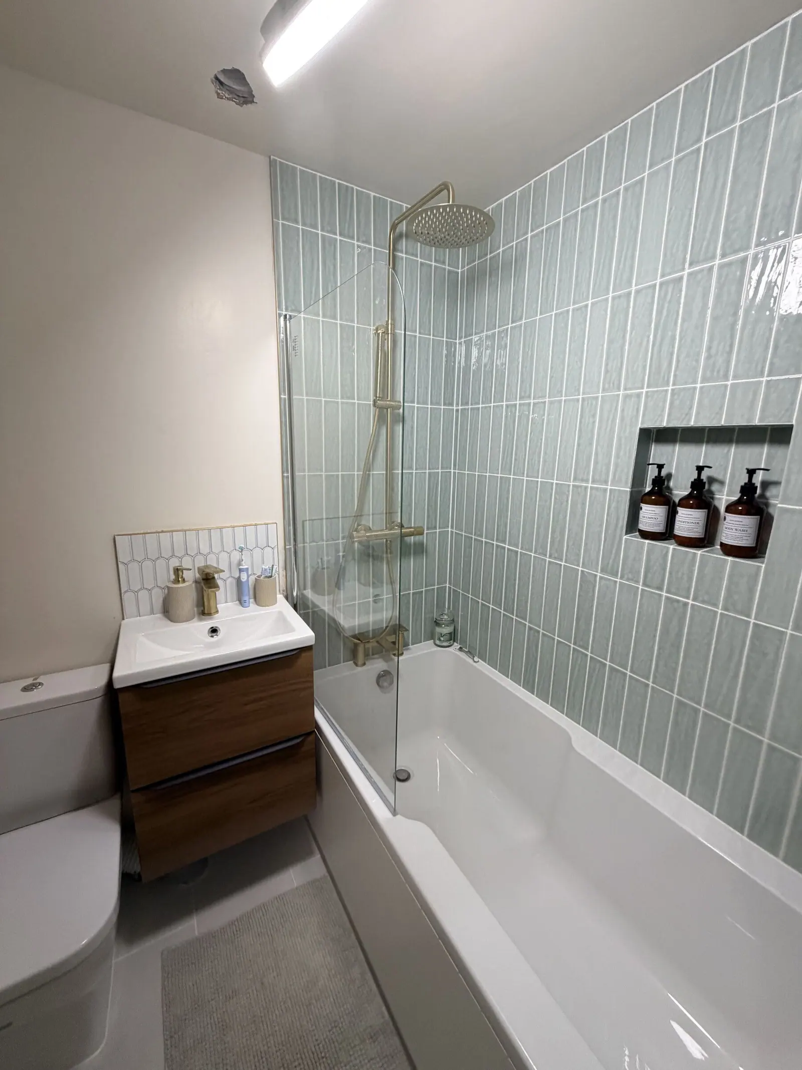 Bathroom with sage green vertical stacked tiles, brushed brass shower, tiled niche and walnut vanity, fitted by Basingstoke Bathrooms