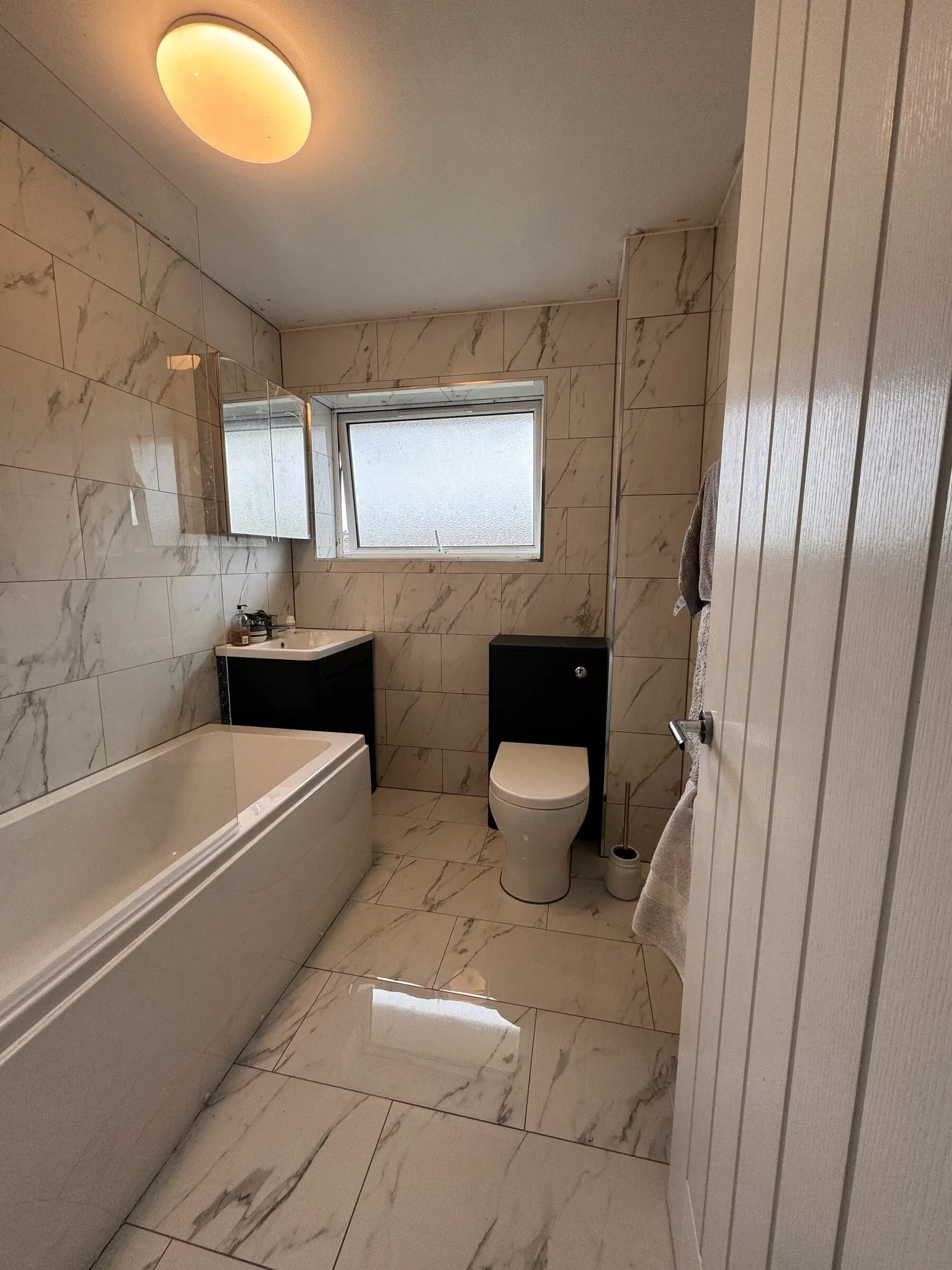Bathroom tiled floor to ceiling in white marble-effect porcelain with a navy vanity and matching WC unit, fitted by Basingstoke Bathrooms
