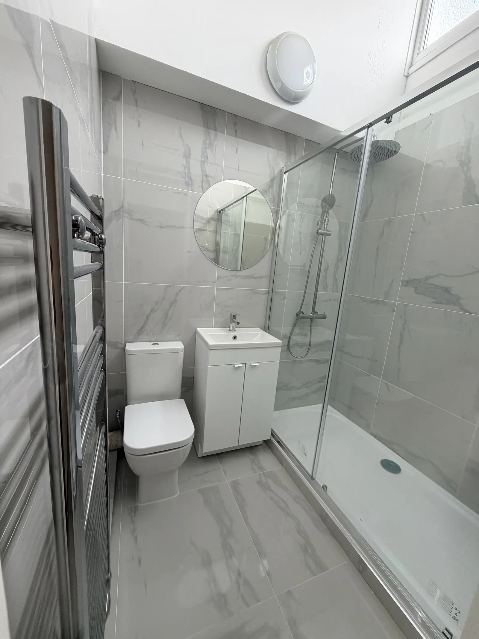 En-suite in white marble-effect tiles with sliding-door shower enclosure, white vanity and round mirror, fitted by Basingstoke Bathrooms